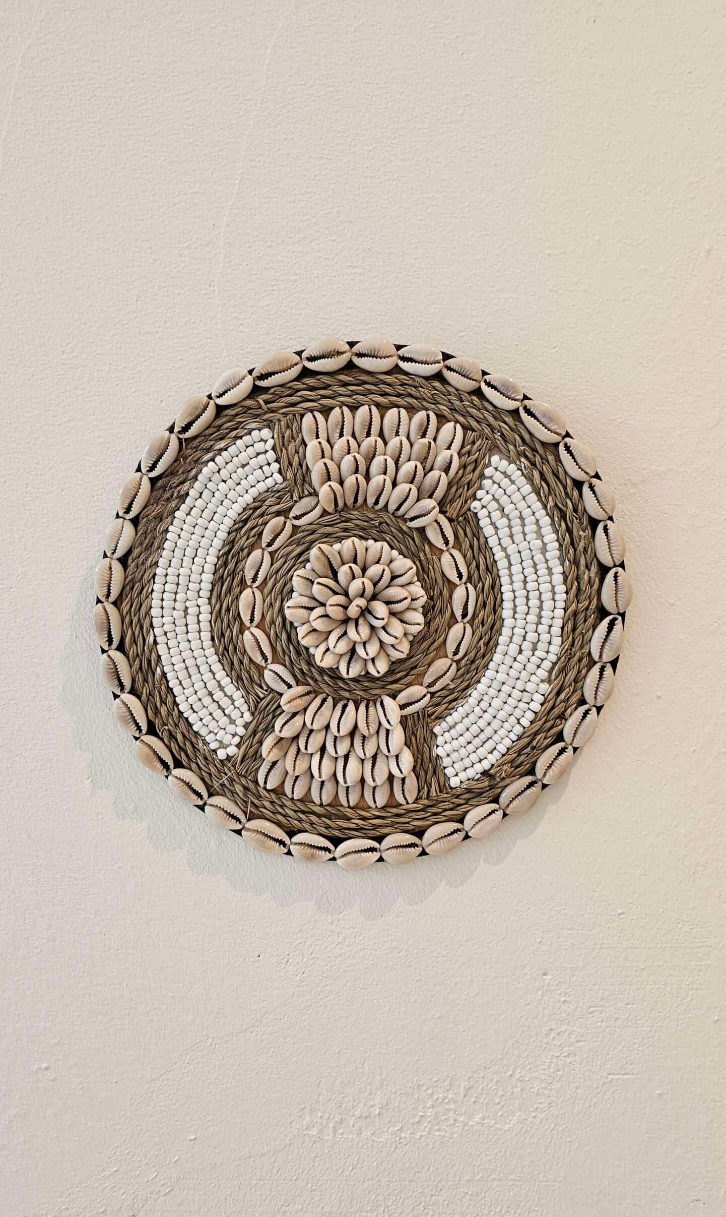 Ronde wanddecoratie van kralen en schelpen in de kleuren wit en beige.