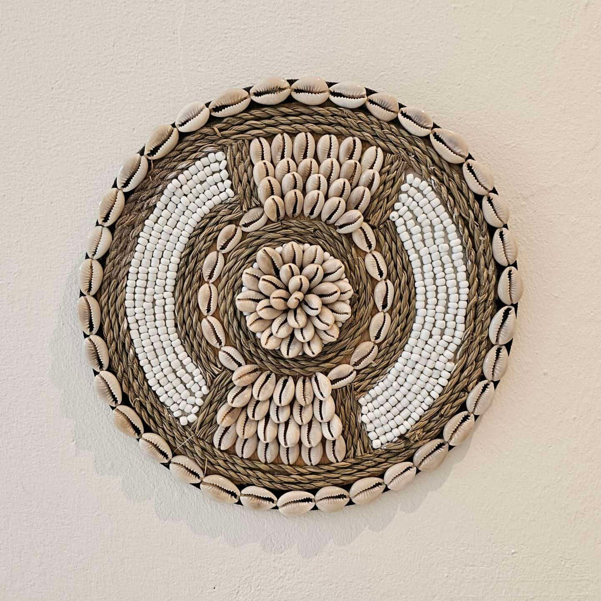 Ronde wanddecoratie van kralen en schelpen in de kleuren wit en beige.