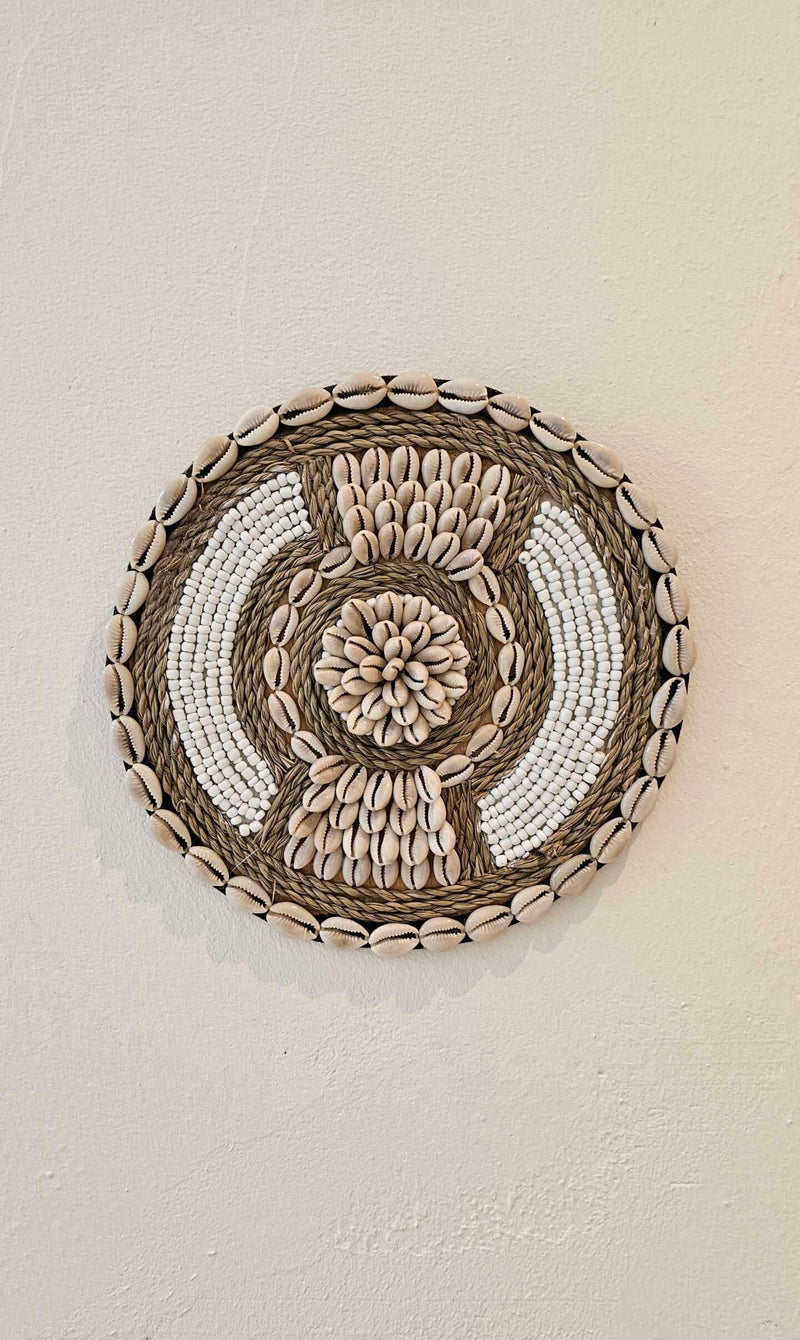 Ronde wanddecoratie van kralen en schelpen in de kleuren wit en beige.