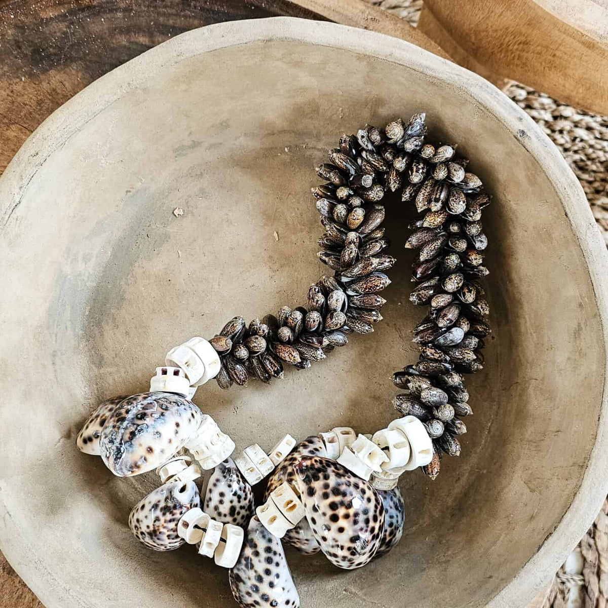 Boho woonketting gemaakt van schelpen ligt in terracotta schaal