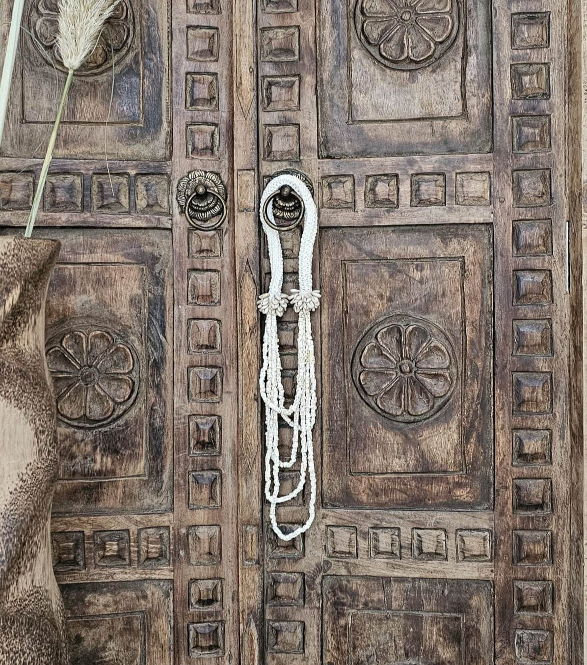 witte schelpenketting uit bali hangt aan houten deur