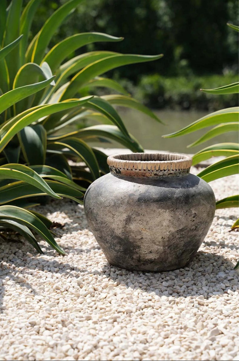 grote boho betonnen vaas met rand van raffia staat buiten naast planten