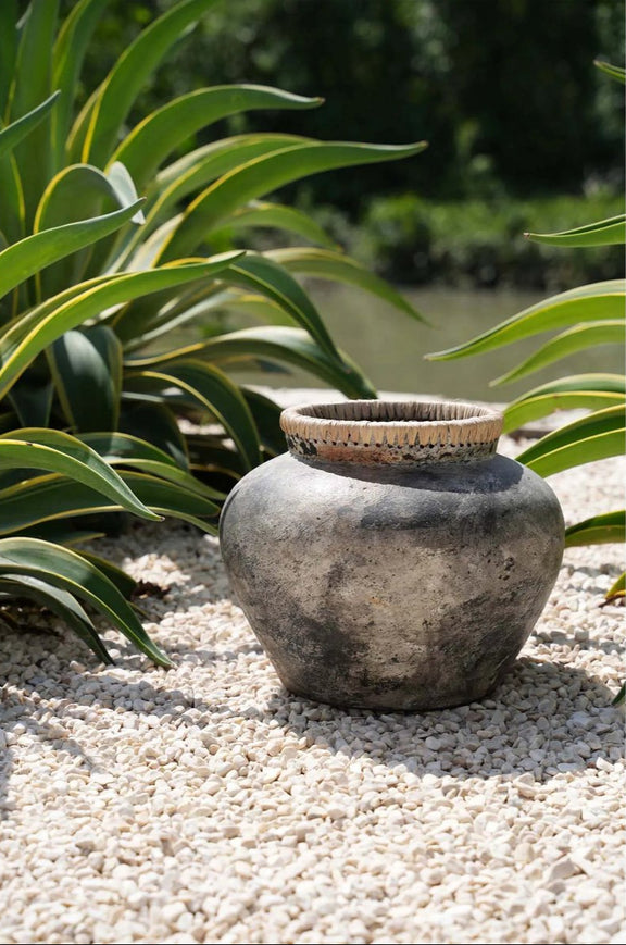grote boho betonnen vaas met rand van raffia staat buiten naast planten